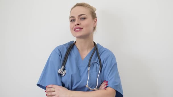 Vrouwelijke arts in blauwe medische jas staat geïsoleerd met gekruiste armen. Kijkend naar camera — Stockvideo