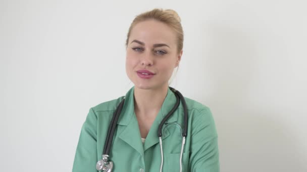 Sorrindo médico fêmea em casaco médico verde com braços cruzados posando olhando para a câmera contra o branco — Vídeo de Stock