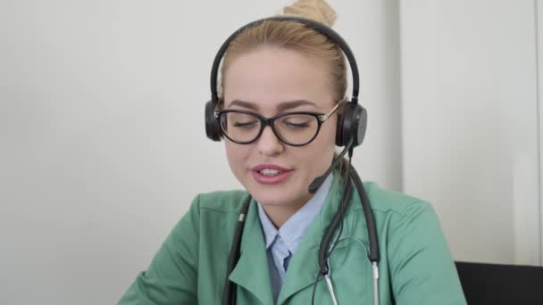 Kobieta lekarz za pomocą zestawu słuchawkowego i prowadzenia rozmowy z pacjentem — Wideo stockowe