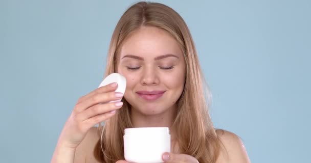 Belle femme caucasienne posant en fond bleu. Elle aime l'odeur de crème hydratante naturelle — Video