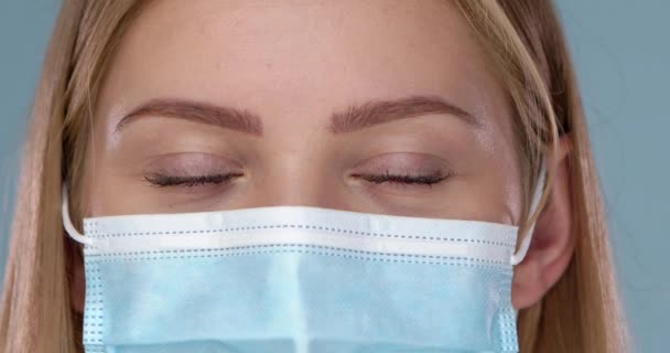 Close-up en gewas frame van jonge vrouw poseren in medische masker. Kijkend naar camera met glimlach — Stockvideo