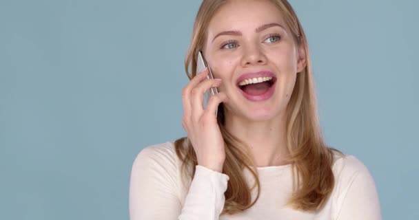 Söt glad ung kvinna pratar med någon på sin smartphone. Isolerad över en blå — Stockvideo