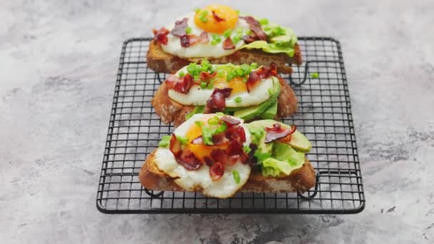 Heerlijke zelfgemaakte toast met gebakken ei, spek, avocado, sla en bieslook. Geserveerd op grill — Stockvideo