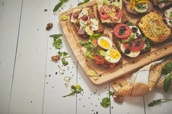 Roti lapis kecil buatan sendiri yang lezat dengan berbagai bahan yang disajikan pada papan potong kayu — Stok Foto
