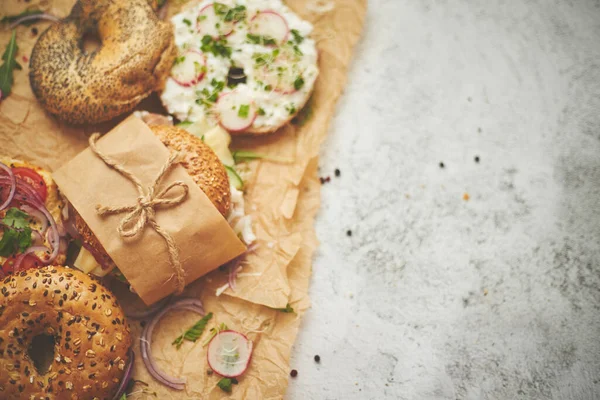 Bagels con jamón, queso crema, hummus, rábano envuelto en papel de hornear marrón listo para llevar — Foto de Stock
