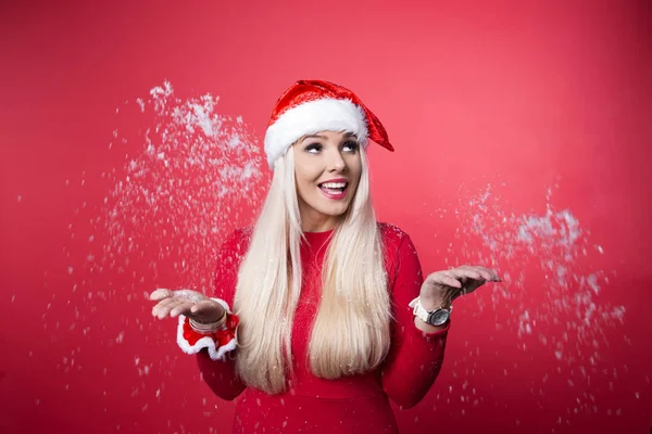 Close up portrait of beautiful sexy girl wearing santa claus clothes with snow in her hands, over red background — Stock Photo, Image