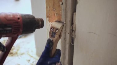 Eski beyaz boyayı ısı tabancası ve kazıyıcı ile kapı çerçevesinden çıkarmanın ayrıntıları.