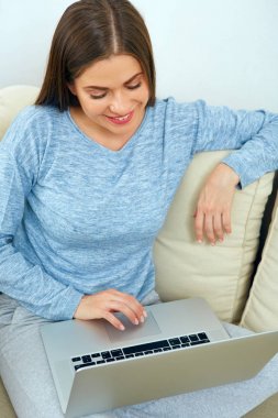 Dizüstü bilgisayar ile kanepede oturan genç kadın.