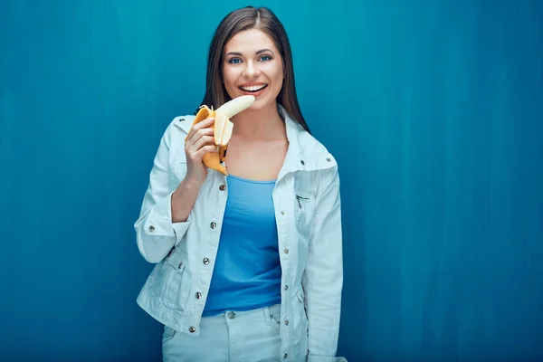 Smiling woman eating banana. Blue background.