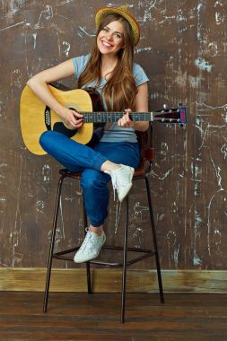 Akustik gitar çalmaya gülümseyen genç kadın.