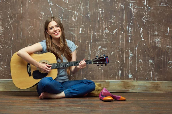 Glad flicka sitter på golvet med akustisk gitarr. — Stockfoto