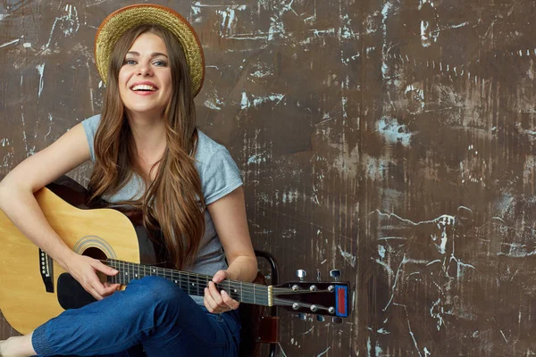Gelukkig jonge vrouw met hoed zitten met akoestische gitaar op grung — Stockfoto