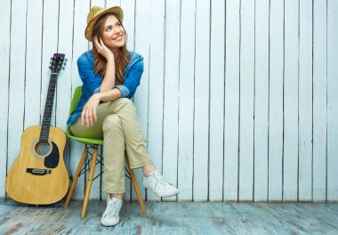 Gülümseyen genç kadın gitar ile oturuyordu