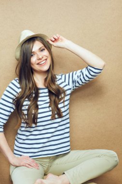 Çizgili kıyafetler ve bej duvar arka plan oturan hipster şapka giyen kadın 