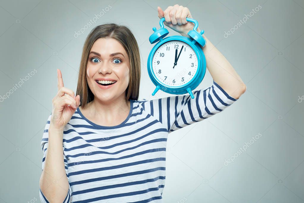 Young woman holding clock and finger against lips.
