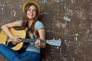 Akustik gitar çalmaya gülümseyen genç kadın.