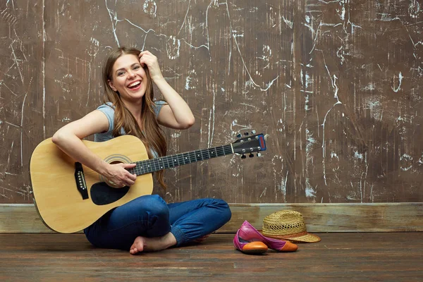 Glad flicka sitter på golvet med akustisk gitarr. — Stockfoto