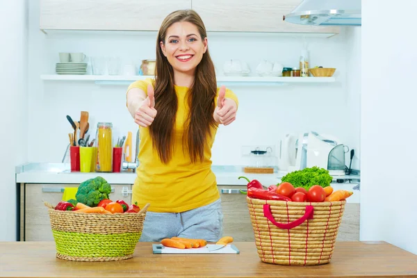 Young woman standing in kitchen with wegetables show thumb up. — Stock Photo, Image