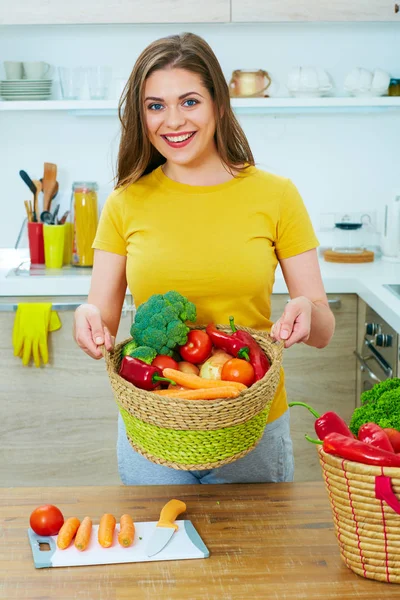 Sonriente mujer de pie en la cocina celebración de la cesta con verduras — Foto de Stock