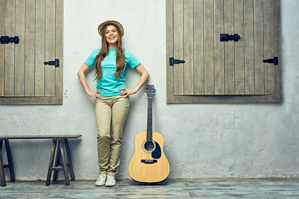 Woman with guitar leaning on light wall — Stock Photo, Image