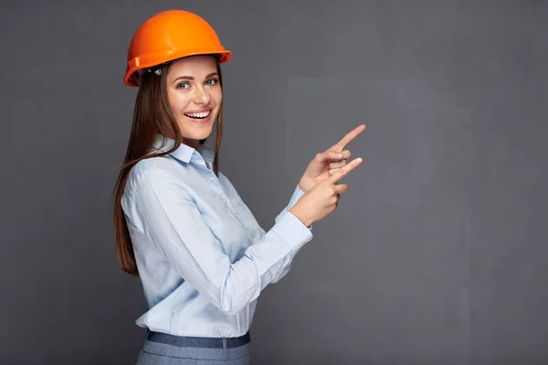 Mujer con casco constructor apuntando con el dedo hacia atrás espacio de copia — Foto de Stock