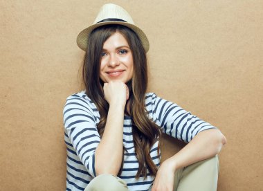 Çizgili kıyafetler ve bej duvar arka plan oturan hipster şapka giyen kadın 