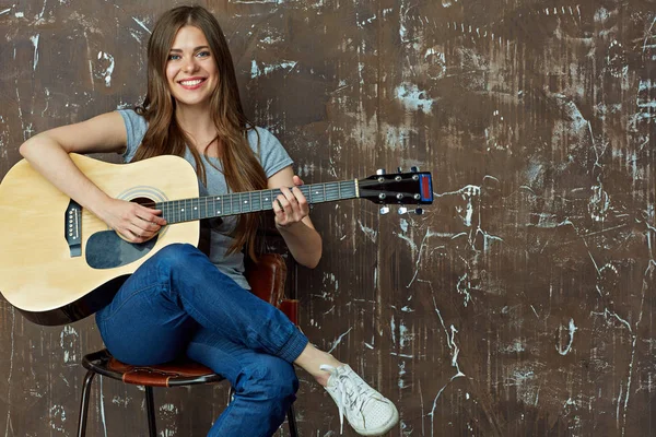 Uśmiechnięta kobieta siedzi i gra na gitarze — Zdjęcie stockowe