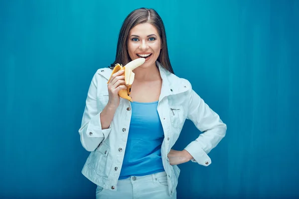 Mujer sonriente comiendo plátano sobre fondo azul . — Foto de Stock