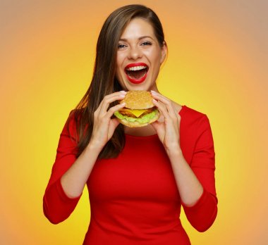 sarı arka plan üzerinde burger ısırma kırmızı elbiseli mutlu kadın 