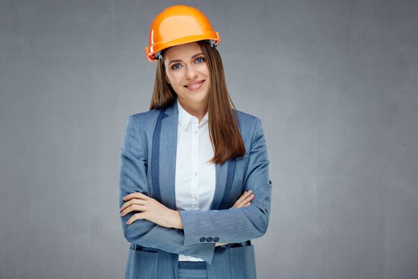 woman builder engineer in business suit standing with crossed arms against gray wall 