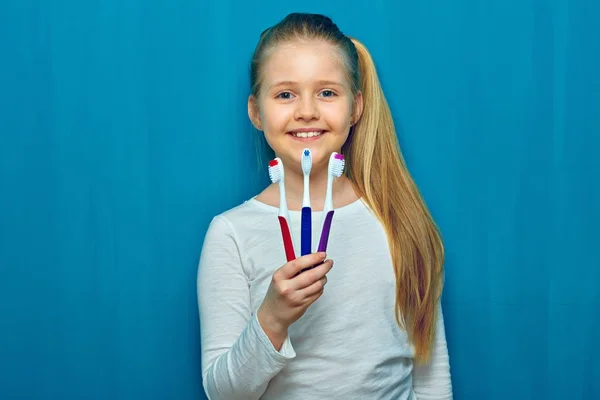 Leende kid flicka håller tre toothy borste. Porträtt på blå — Stockfoto