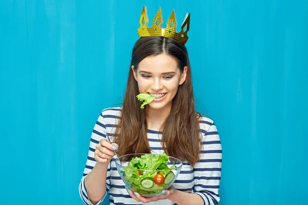smiling young woman with crown on head eating diet food green salad, healthy food concept