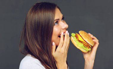Genç kadın Burger hızlı yemek yeme. Gri duvar karşı izole portre.