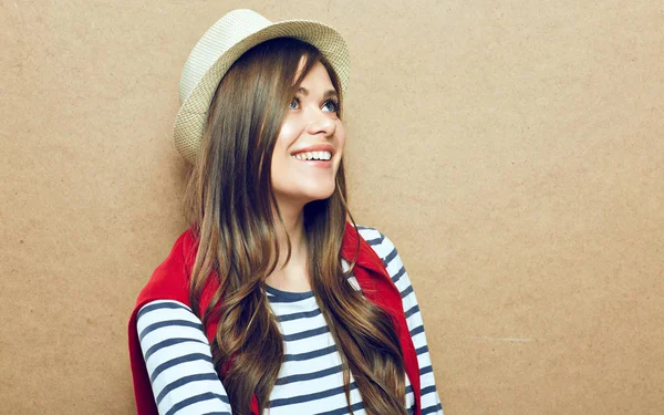 woman wearing striped shirt and hipster hat sitting near beige wall background