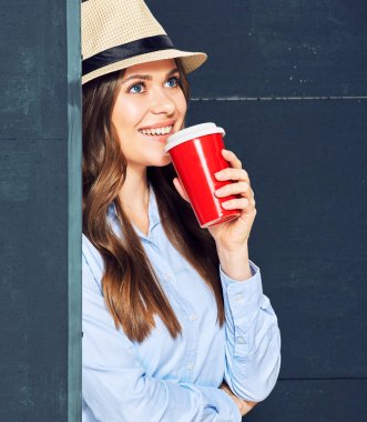 genç kadın kırmızı fincan kahve içme ve siyah duvara yakın duran şapkalı 