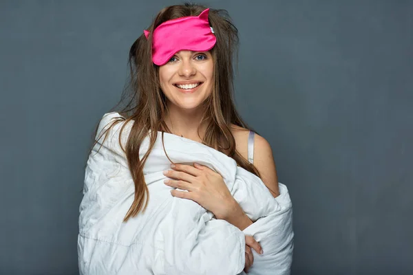 smiling woman with sleep mask wearing white blanket, healthy sleep concept