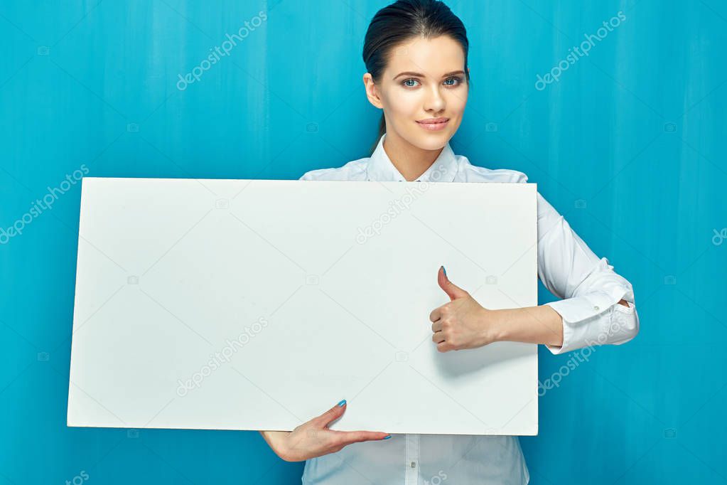 smiling woman holding big white sign board and showing thumb up on blue wall background