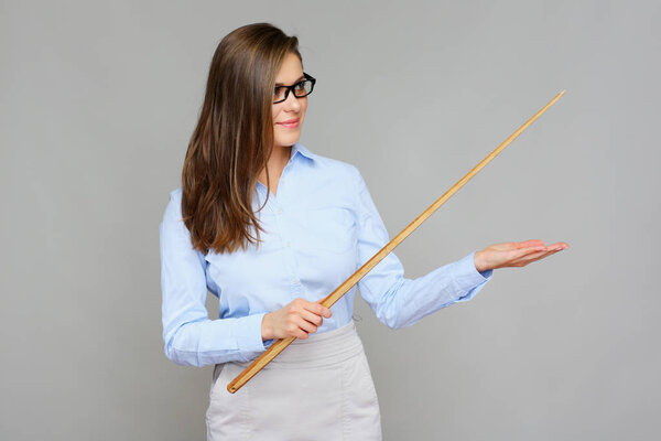 portrait of young teacher wearing glasses holding wooden pointer and showing empty hand on grey background, education concept 