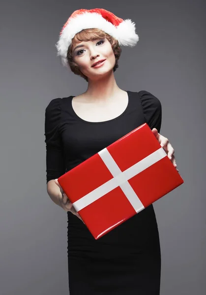 微笑的年轻女子在圣诞老人的帽子摆着红色礼品盒 — 图库照片