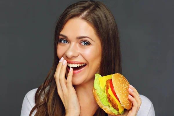 portrait of happy woman eating burger on grey background, fast food concept