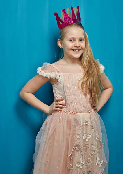 Smiling girl wearing pink dress standing against blue wall. — Stock Photo, Image