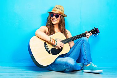 moda müzik bak genç bir model mavi katta oturan ve akustik gitar çalmak şapka ve güneş gözlüğü ile 