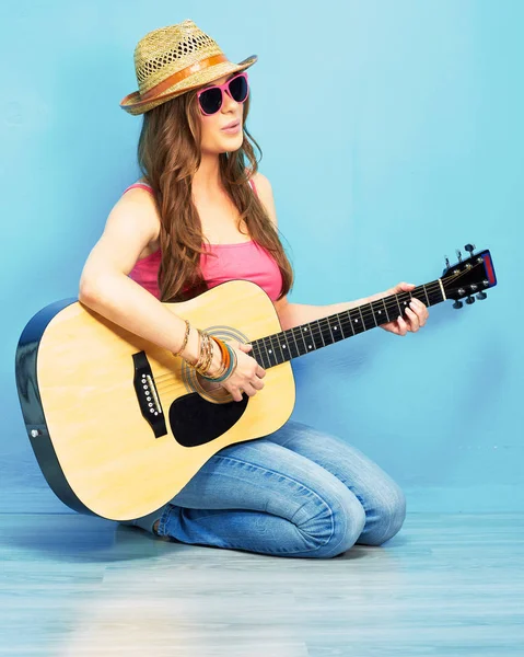 时尚音乐与年轻模特在太阳镜和帽子坐在蓝色的地板和演奏原声吉他 — 图库照片