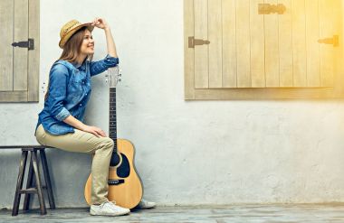 Akustik gitar sokak ışık duvarının yakınında oturan genç kadın gitarist