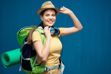 Gülümseyen kadın şapka zekâ sırt çantası ve kulaklık mavi duvar arka plan üzerinde seyahat kavramı 