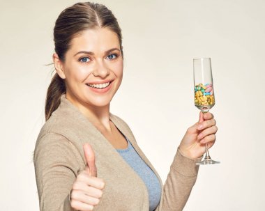 Kadehinin vitamin hapları ile tutarak ve başparmak karşı karşıya bej renkli arka plan üzerinde gösterilen genç kadın 