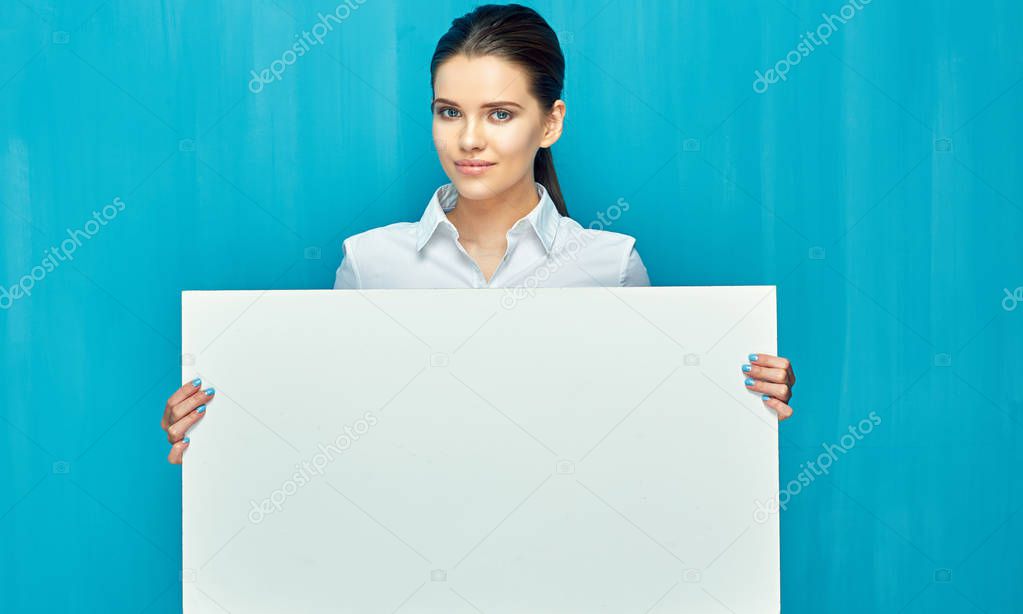 smiling businesswoman wearing white shirt holding advertising banner in hands on blue wall background