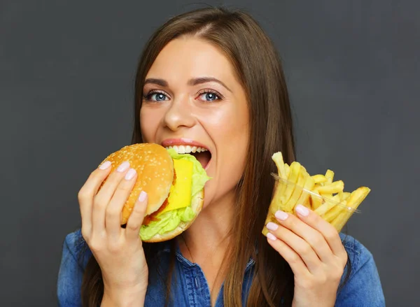 笑顔の女性ブルー ジーンズ シャツかむハンバーガーとフライド ポテトを保持 — ストック写真