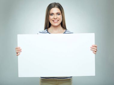 Boş beyaz reklam afişi gri arka plan üzerinde tutarak çizgili gömlek gülümseyen kadın