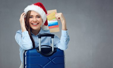 Noel giyen gülümseyen kadın kış tatil kavramı seyahat biletleri ve kredi kartı süre eğilerek bavul üzerinde tutarak Noel Baba şapkası 